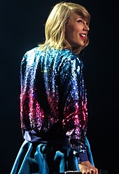 Swift performing onstage wearing a blue skirt and sparkling jacket