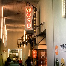 A large vertical sign reading W O S U over an exhibit space in an indoor hallway
