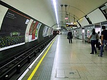 A wide concrete platform in a circular tunnel. Railway track runs along the left with posters fixed to the wall opposite the platform.