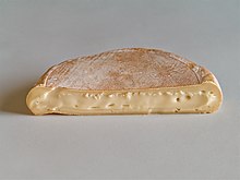 Half-circle of soft tan cheese, cut side forward, on white table