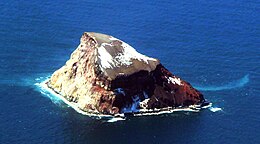 A red-brown-yellow rock rising from the sea