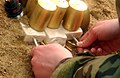 Inserting blasting caps into blocks of C-4 explosive (bottom) being used to destroy unexploded artillery components (cylinders)