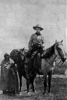 Ein schwarz-weiss Foto zeigt einen sehr jungen Mann zu Pferd in einem Cowboy-Dress mit voll beladenem Packpferd.