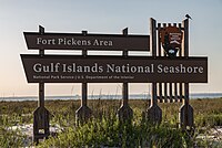 Wooden sign saying "Fort Pickens Area, Gulf Islands National Seashore" standing in front of a beach at sunset