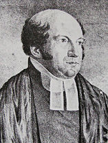 The Reverend Richard Hill is a chubbier man of middle age, with a very bald head fringed with dark curling hair. He wears parson's bands (two white tags at his neck).