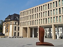 Das Bild zeigt den Campusplatz der TU Darmstadt in der Stadtmitte mit dem Gebäude der Universitäts- und Landesbibliothek, dem Wickopflügel des Alten Hauptgebäudes sowie der Skulptur „Büste“ von Franz Bernhard.
