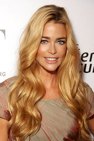 A woman with long blonde hair with a grey dress smiles toward the camera.