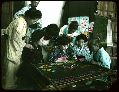 Group of women and one man watching young woman working on large embroidery
