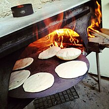 Six pitas baking on a circular pan in a wood-fired oven