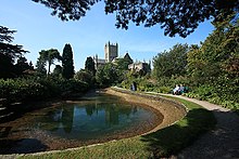 Pool of water in an area of trees and shrubs. In the background is the cathedral.