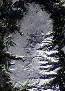 An overhead view of an oval-shaped, snow-covered plateau with a snow-covered mountain in the middle.