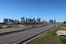 A skyline of tall buildings viewed from an overpass of a freeway