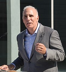Man in a suit giving a outdoors speech at a podium