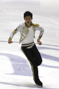 A photograph of a young Nathan Chen in a white, gold and black costume, performing to music by Michael Jackson.