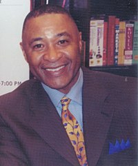 Man wearing a suit with a blue shirt. He has a crew-cut haircut.
