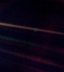 A tiny, pale blue dot is contrasted against the vastness of space