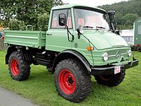An civilian Unimog 406 truck painted in pastel colours in front of a forest background.