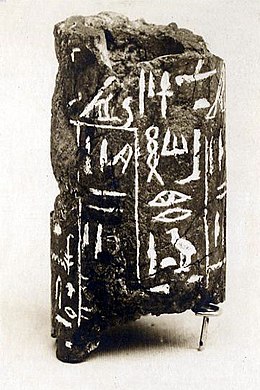 Broken cylinder of dark grey stone with white hieroglyphs inscribed on it