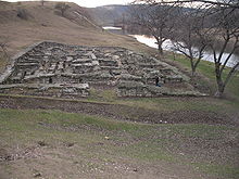 Large, low stone construction (with people walking past for scale) near a river