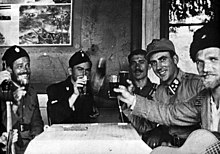 A black and white photograph of uniformed males seated around a table, with several holding glasses