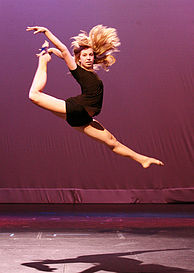 A contemporary dancer performs a stag split leap.