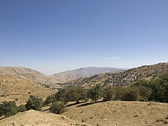 Photo of arid hills with sparse vegetation and trees in the foreground