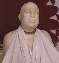 A face close-up of a marble statue of a man with wooden beads and white cloth around the neck.