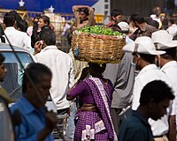 A woman carrying a basket full of vegetables on her head in K R Market, Bangalore, India