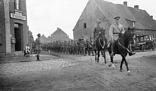 a black and white photograph of a mounted officer leading troops on foot