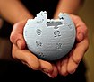 two hands cupped together extended toward camera holding Wikipedia globe