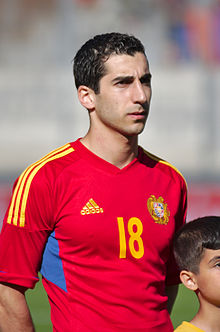 A man with dark hair wearing a red football jersey with yellow trim.