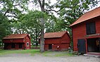 Three red wooden buildings from the 19th century with orange roofs.