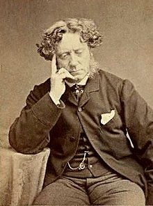 Monotype photograph of Sir Joseph Noel Paton. He seated beside a table, wearing a suit, resting his chin on his right hand.