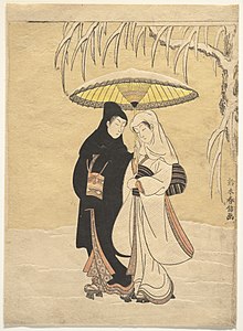 A man and a woman dressed in kimono and headscarves walk through the snow.