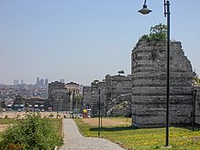 Photograph of a city scene; large, ruined walls can be seen to the right.