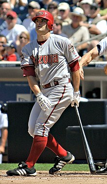 A man in red socks and a gray baseball uniform with "Arizona" on the chest stands after taking a right-handed baseball swing.