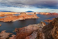 Aerial view of tall red rock mesas rising above the reservoir with a cloudy sky