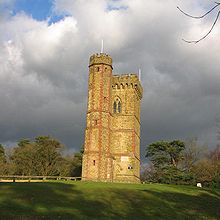 beige stone tower with cylindrical tower attached standing on a grassy hill