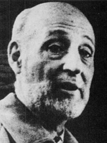 A black-and-white image of a middle-aged bald man who is speaking