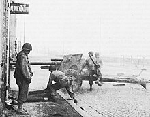 Black and white photograph of soldiers with an artillery gun next to a building