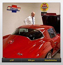 Biden stands beside a red vintage car in a garage.