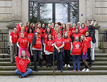 35 Frauen in roten T-Shirts stehen als Gruppe auf einer Treppe vor einer Glastür