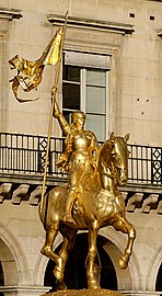 Gold statue of Joan of Arc holding flag and riding horse