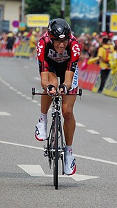 A cyclist on his bicycle, wearing a red and black jersey with white trim.