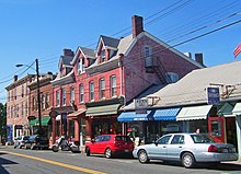 A two-lane highway with an additional lane for street parking is flanked by shops housed in old buildings.