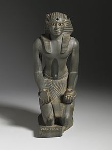 Grey statue of kneeling pharaoh, with vases in its hands