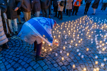 Das Foto zeigt eine Person mit Flagge Israels, die eine Kerze zu dem Kerzenmeer stellt