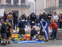 Football fans in kilts and other tartan garb, mixed with informal everyday clothing, on steps outside an arena