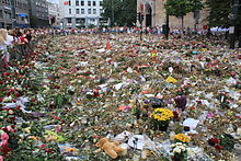 Foto einer Menschenmenge hinter niedergelegten Blumen und Kerzen