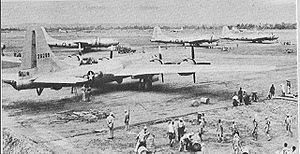 Four large 4-engined World War II-era aircraft sitting on the ground at an airstrip. Groups of people are working near each aircraft.